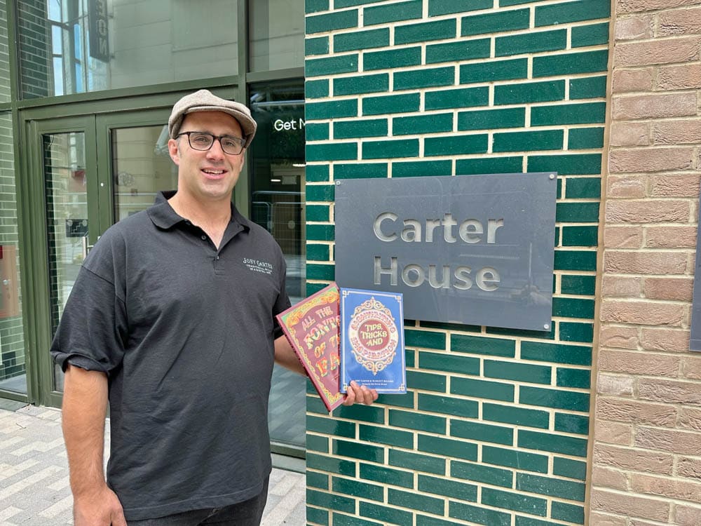 Joby Carter standing outside Carter House with his two books