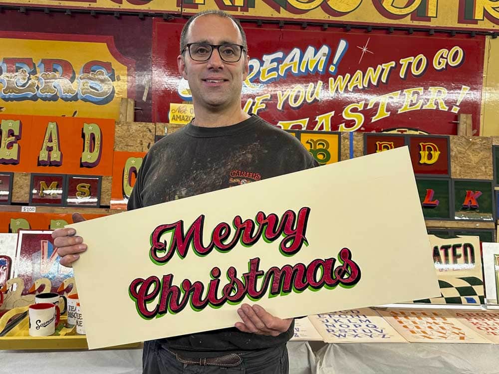Joby Carter holding a hand painted Merry Christmas sign