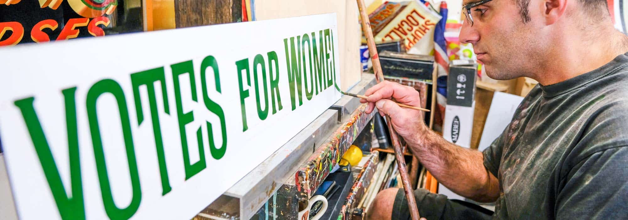 Joby Carter signwriter paining a 'votes for women' sign