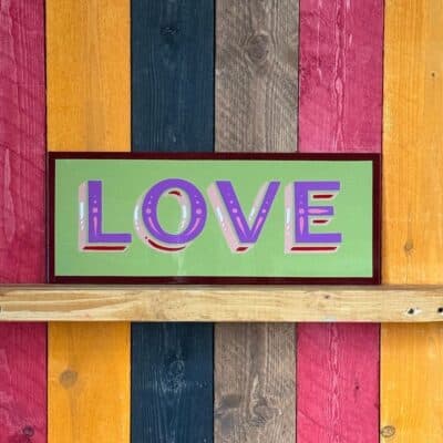 Rectangular sign with the letter LOVE painted in purple with a green background